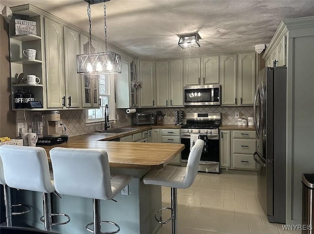 kitchen featuring open shelves, a sink, a kitchen bar, a peninsula, and stainless steel appliances