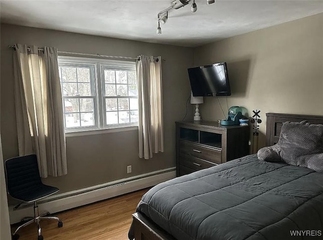 bedroom with a baseboard radiator, wood finished floors, and baseboards
