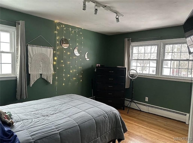 bedroom featuring multiple windows, wood finished floors, and baseboard heating