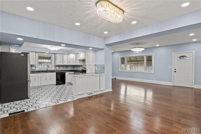 kitchen featuring black dishwasher, a sink, open floor plan, freestanding refrigerator, and a chandelier