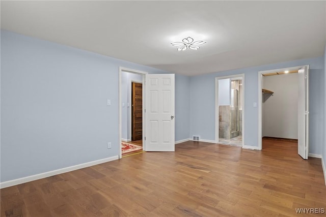 unfurnished bedroom with a closet, baseboards, a walk in closet, and wood finished floors