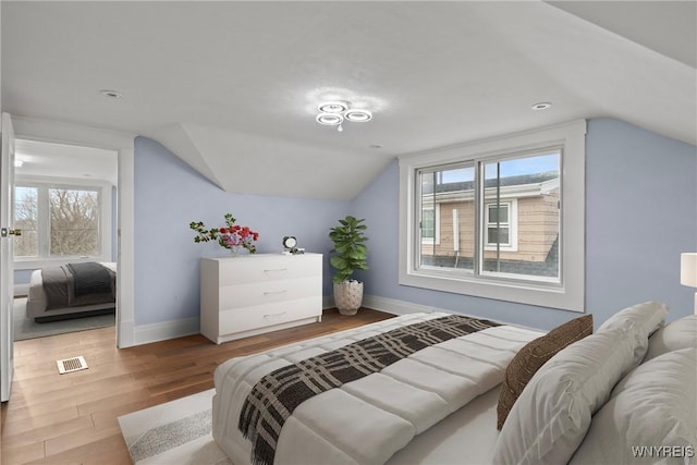 bedroom with wood finished floors, visible vents, baseboards, and lofted ceiling