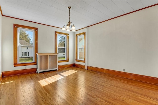 spare room featuring baseboards, an inviting chandelier, crown molding, radiator heating unit, and hardwood / wood-style floors