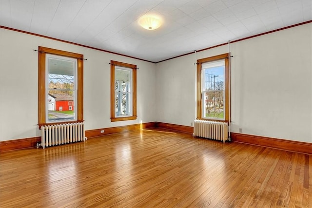 empty room featuring a healthy amount of sunlight, radiator heating unit, and wood-type flooring