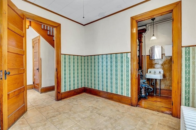 unfurnished room featuring crown molding, wallpapered walls, baseboards, and wainscoting