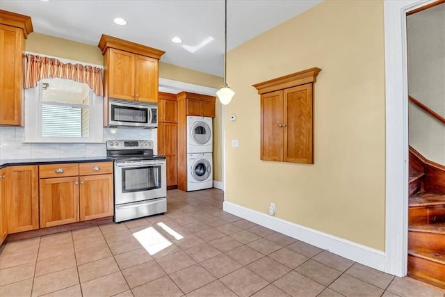 kitchen with light tile patterned floors, dark countertops, stainless steel appliances, decorative light fixtures, and stacked washer and clothes dryer