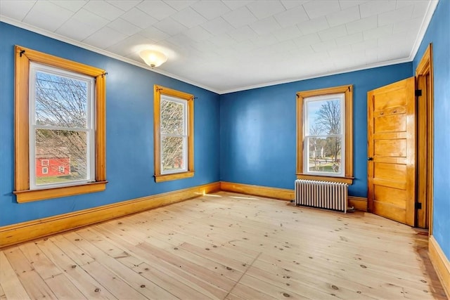 empty room with crown molding, radiator heating unit, baseboards, and a healthy amount of sunlight