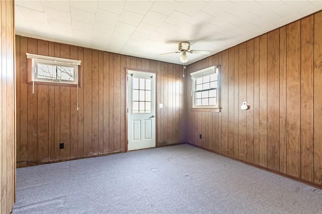 empty room featuring carpet, wooden walls, and ceiling fan