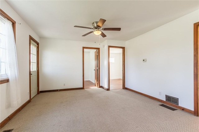 empty room featuring light carpet, visible vents, baseboards, and a ceiling fan