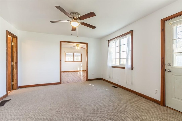 empty room with carpet flooring, baseboards, a ceiling fan, and visible vents