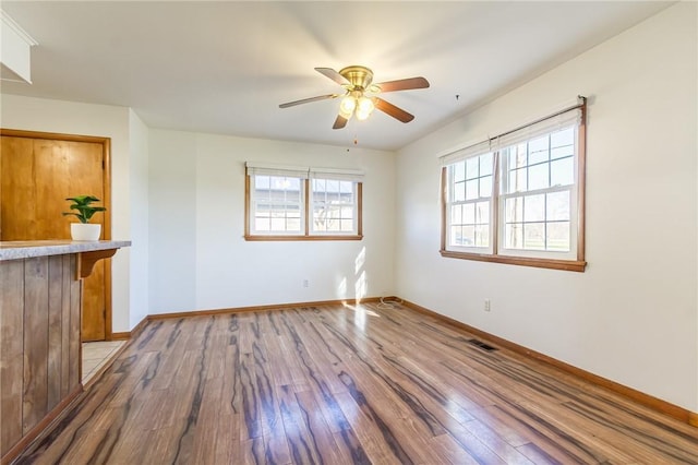 empty room featuring baseboards, hardwood / wood-style floors, a ceiling fan, and a healthy amount of sunlight