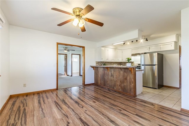 kitchen with light wood-style floors, ceiling fan, freestanding refrigerator, and a peninsula
