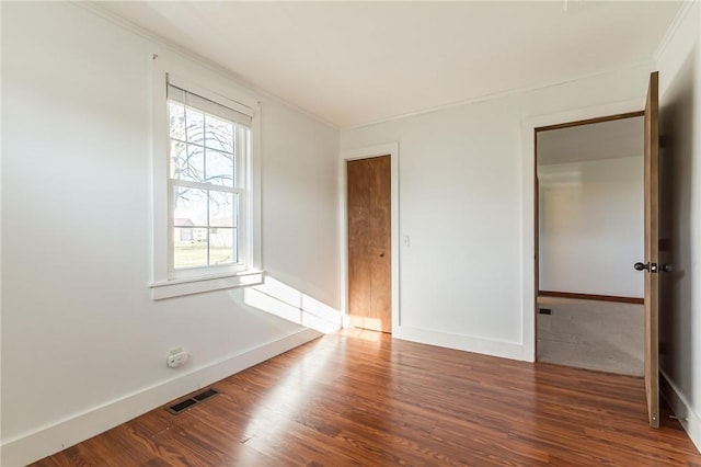empty room with crown molding, wood finished floors, baseboards, and visible vents