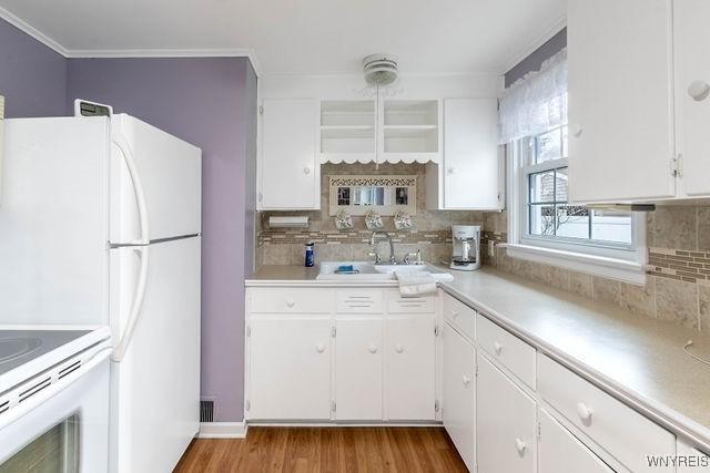 kitchen featuring ornamental molding, white cabinetry, a sink, light countertops, and backsplash