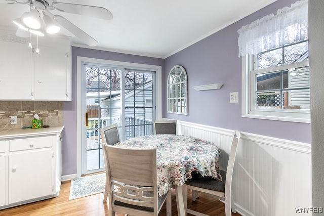 dining room featuring light wood-style floors, ceiling fan, ornamental molding, and wainscoting