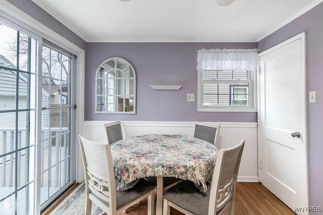 dining space with crown molding, wood finished floors, and a wainscoted wall