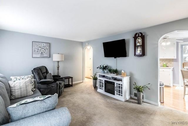 living room with ceiling fan, baseboards, arched walkways, and light colored carpet