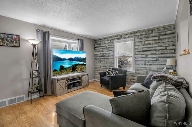living area featuring visible vents, light wood-type flooring, an accent wall, and a textured ceiling