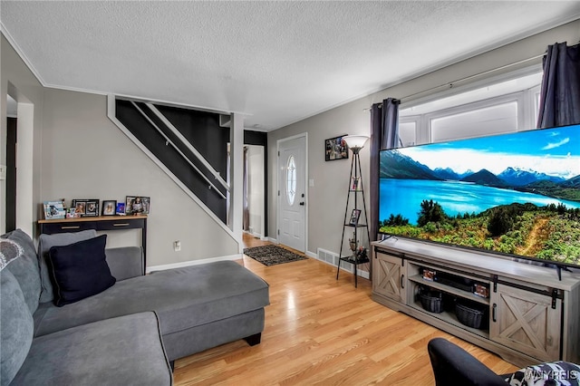 living area with stairway, light wood-style floors, visible vents, and a textured ceiling