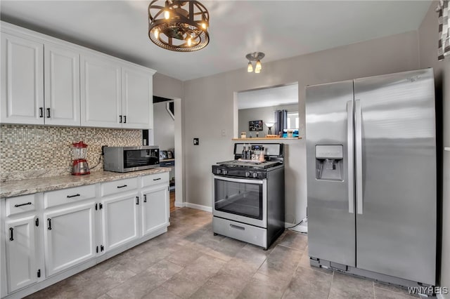 kitchen with tasteful backsplash, white cabinetry, appliances with stainless steel finishes, light stone counters, and baseboards