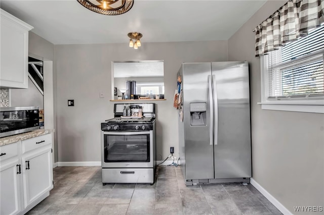 kitchen with stainless steel appliances, plenty of natural light, white cabinets, and baseboards