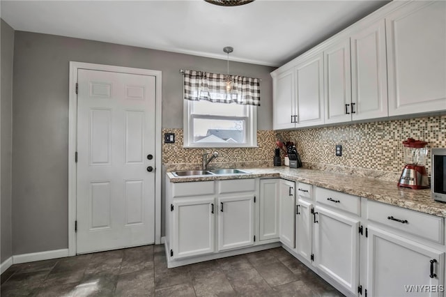 kitchen with tasteful backsplash, white cabinets, a sink, hanging light fixtures, and baseboards