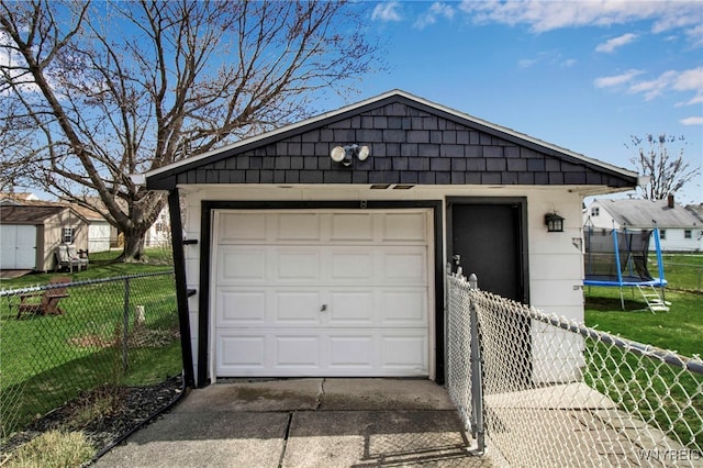 detached garage with a trampoline, concrete driveway, and fence