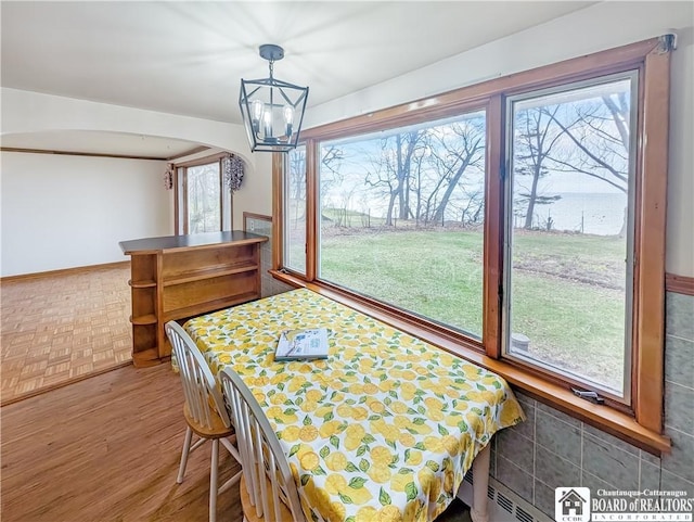 dining space with a notable chandelier, baseboards, a water view, arched walkways, and wood finished floors