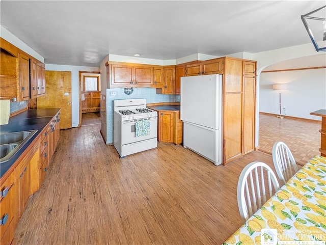 kitchen with arched walkways, tasteful backsplash, white appliances, and light wood-type flooring
