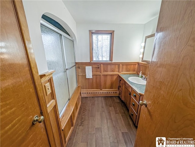 bathroom with combined bath / shower with glass door, a wainscoted wall, hardwood / wood-style floors, and vanity
