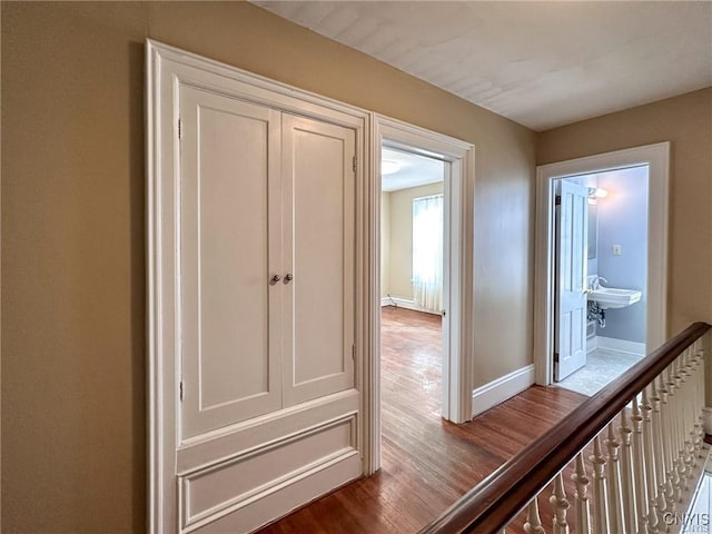 hall featuring wood finished floors, a sink, and baseboards