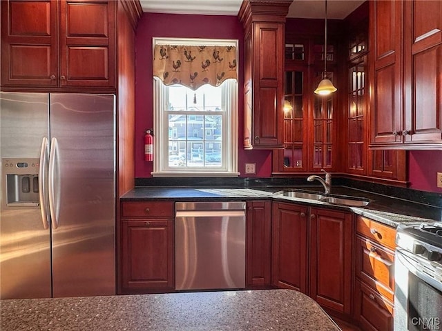 kitchen with glass insert cabinets, decorative light fixtures, a sink, appliances with stainless steel finishes, and reddish brown cabinets