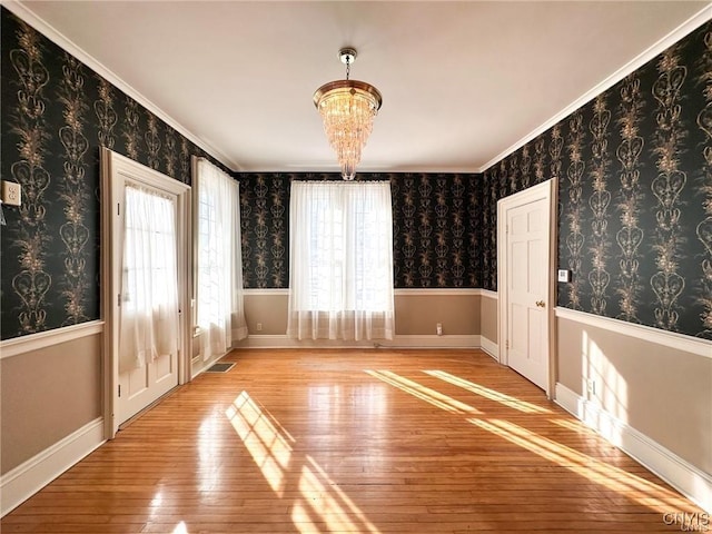 unfurnished room with a wealth of natural light, light wood finished floors, baseboards, and an inviting chandelier