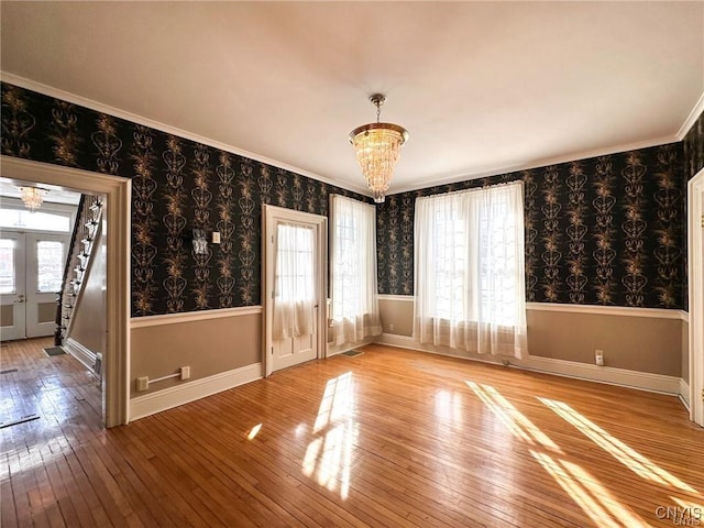empty room with crown molding, wood-type flooring, a notable chandelier, and wallpapered walls