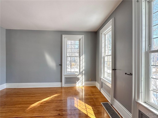 spare room featuring visible vents, a wealth of natural light, wood finished floors, and baseboards