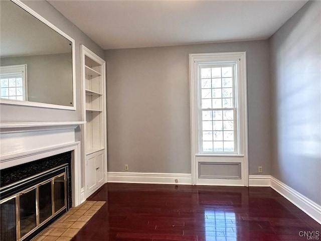 unfurnished living room featuring baseboards, wood finished floors, and a healthy amount of sunlight