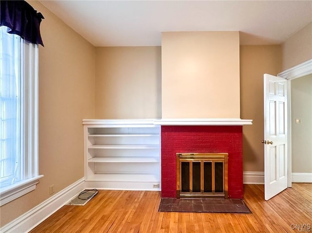 unfurnished living room with a brick fireplace, a wealth of natural light, and wood finished floors
