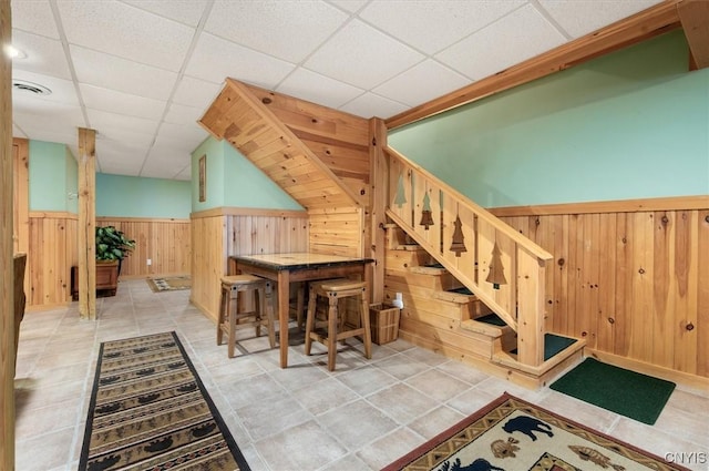interior space featuring wooden walls, a drop ceiling, and a wainscoted wall