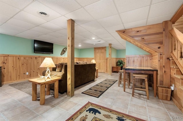 interior space with a drop ceiling, wood walls, wainscoting, and visible vents