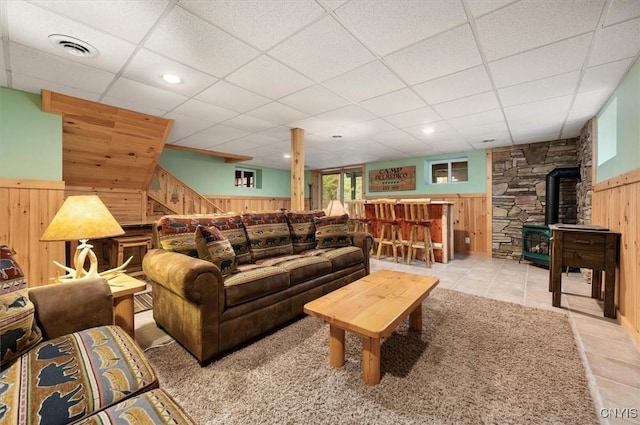 tiled living area featuring wood walls, a wood stove, visible vents, and a drop ceiling