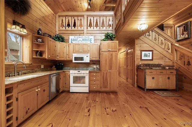 kitchen featuring light brown cabinets, white appliances, wooden walls, light wood finished floors, and a sink