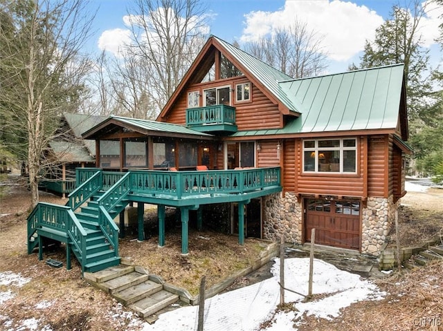 back of property featuring stone siding, an attached garage, stairs, a standing seam roof, and metal roof