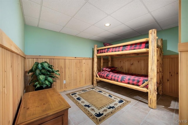 tiled bedroom with wooden walls, a drop ceiling, and a wainscoted wall