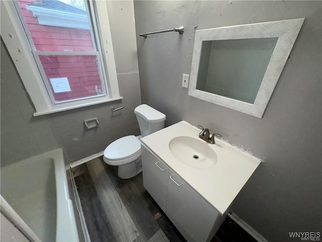 full bathroom with a tub, toilet, vanity, and wood finished floors