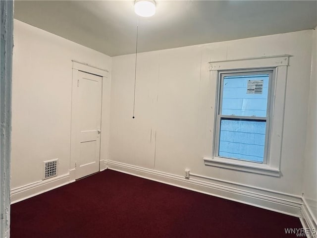 empty room featuring dark colored carpet, visible vents, and baseboards