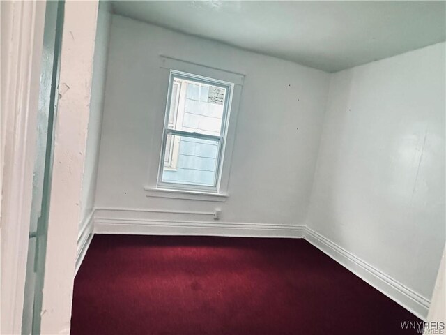 unfurnished room with dark colored carpet and baseboards