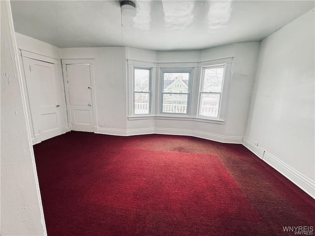 empty room with dark colored carpet, baseboards, and a healthy amount of sunlight