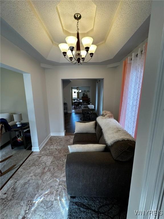 living room featuring a tray ceiling, baseboards, a notable chandelier, and a textured ceiling