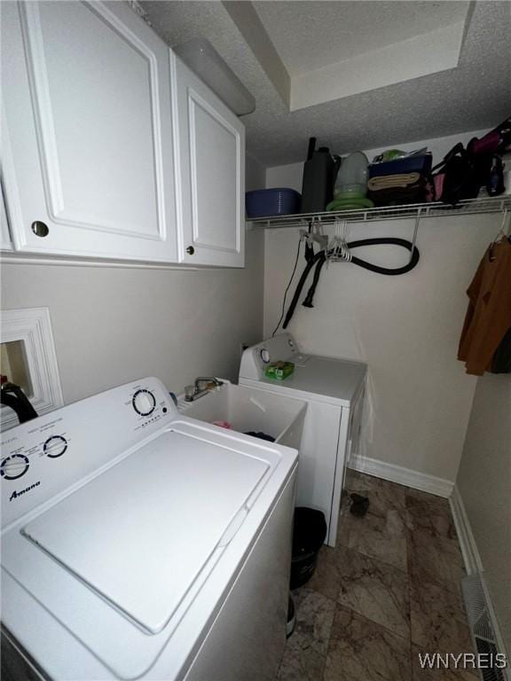 laundry area featuring baseboards, independent washer and dryer, a textured ceiling, and cabinet space