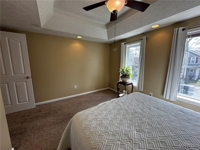 bedroom with baseboards, a ceiling fan, a textured ceiling, a tray ceiling, and carpet flooring
